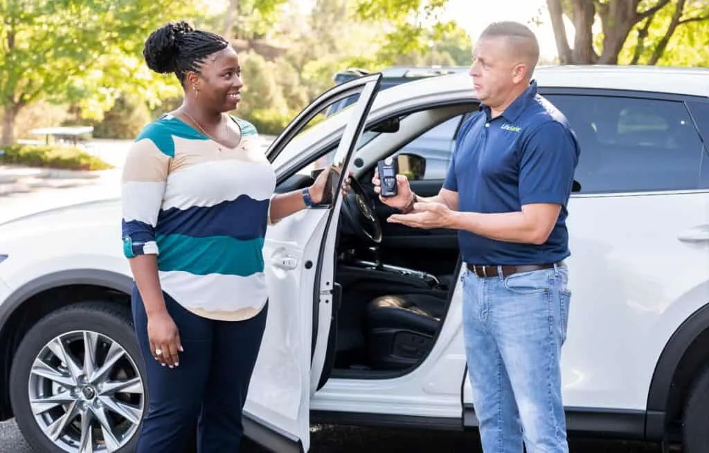 Two individuals standing outside their car, holding a LifeSafer breathalyzer device